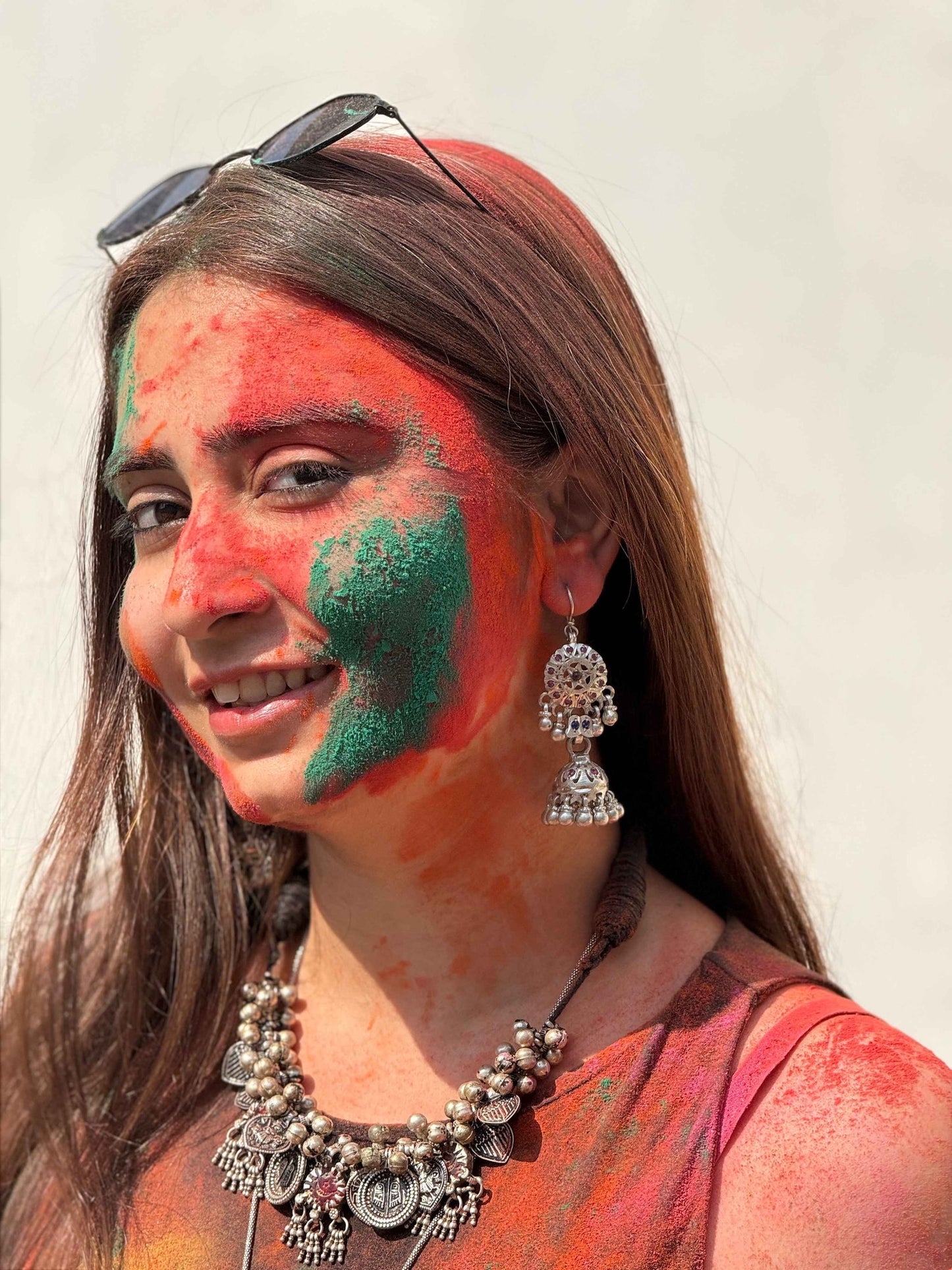 Woman with colorful face paint and traditional silver jewelry against a plain background