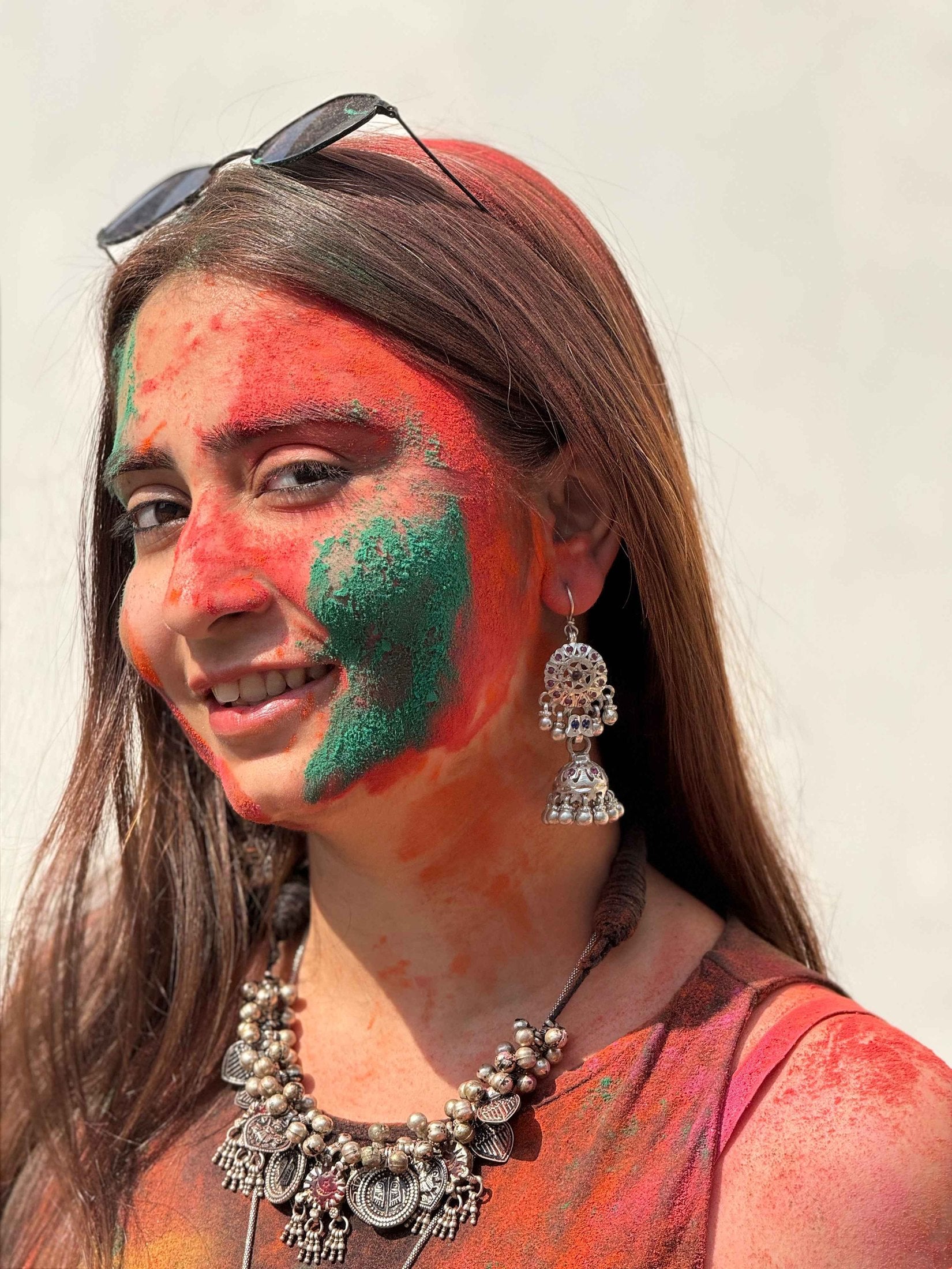 Woman with colorful face paint and traditional silver jewelry against a plain background