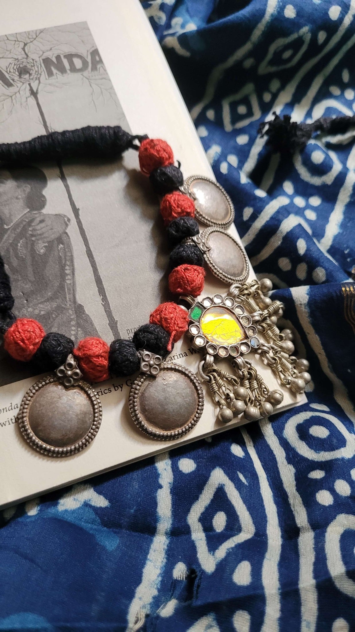 Sunehri Vintage Necklace with red, and black beads and yellow glass pendant on a blue patterned fabric background