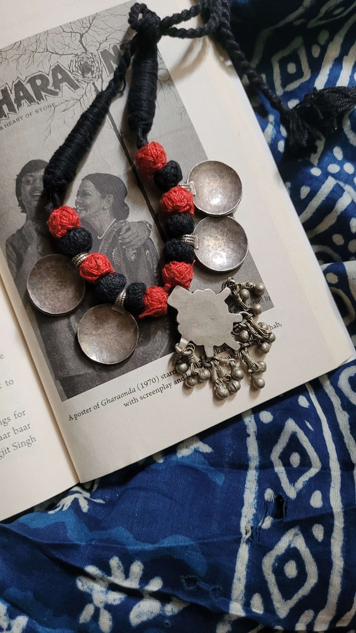 Necklace with red and black floral elements on an open book with a patterned fabric background