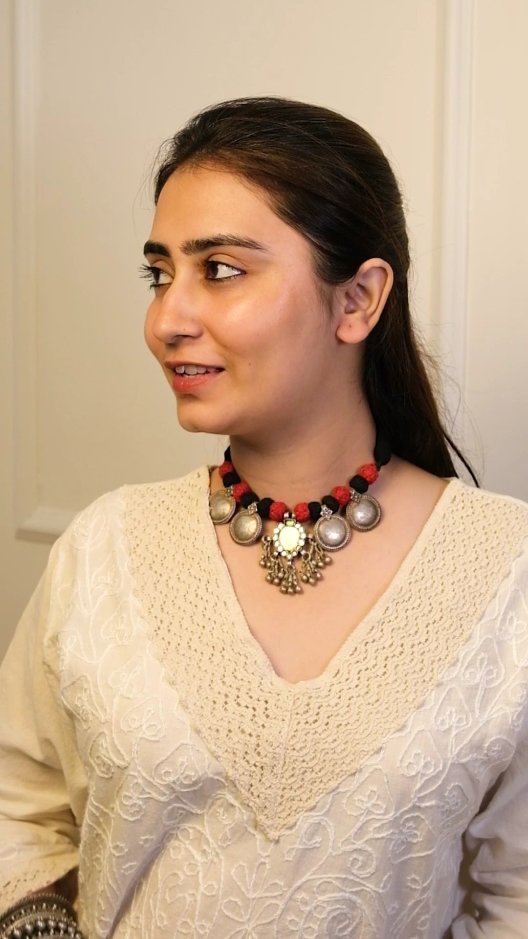 Woman wearing a white traditional outfit with a decorative necklace against a plain background