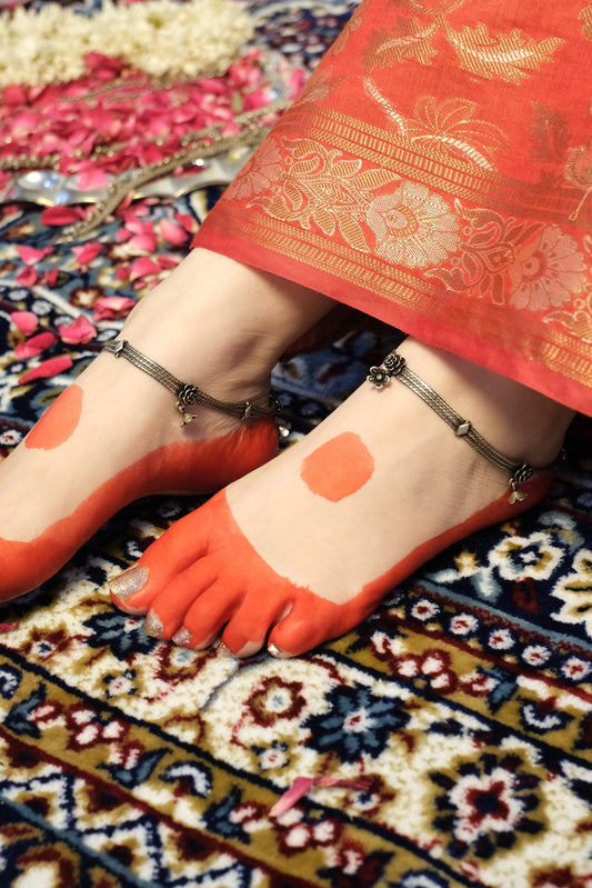 Person wearing red aalta and a red saree on a patterned rug