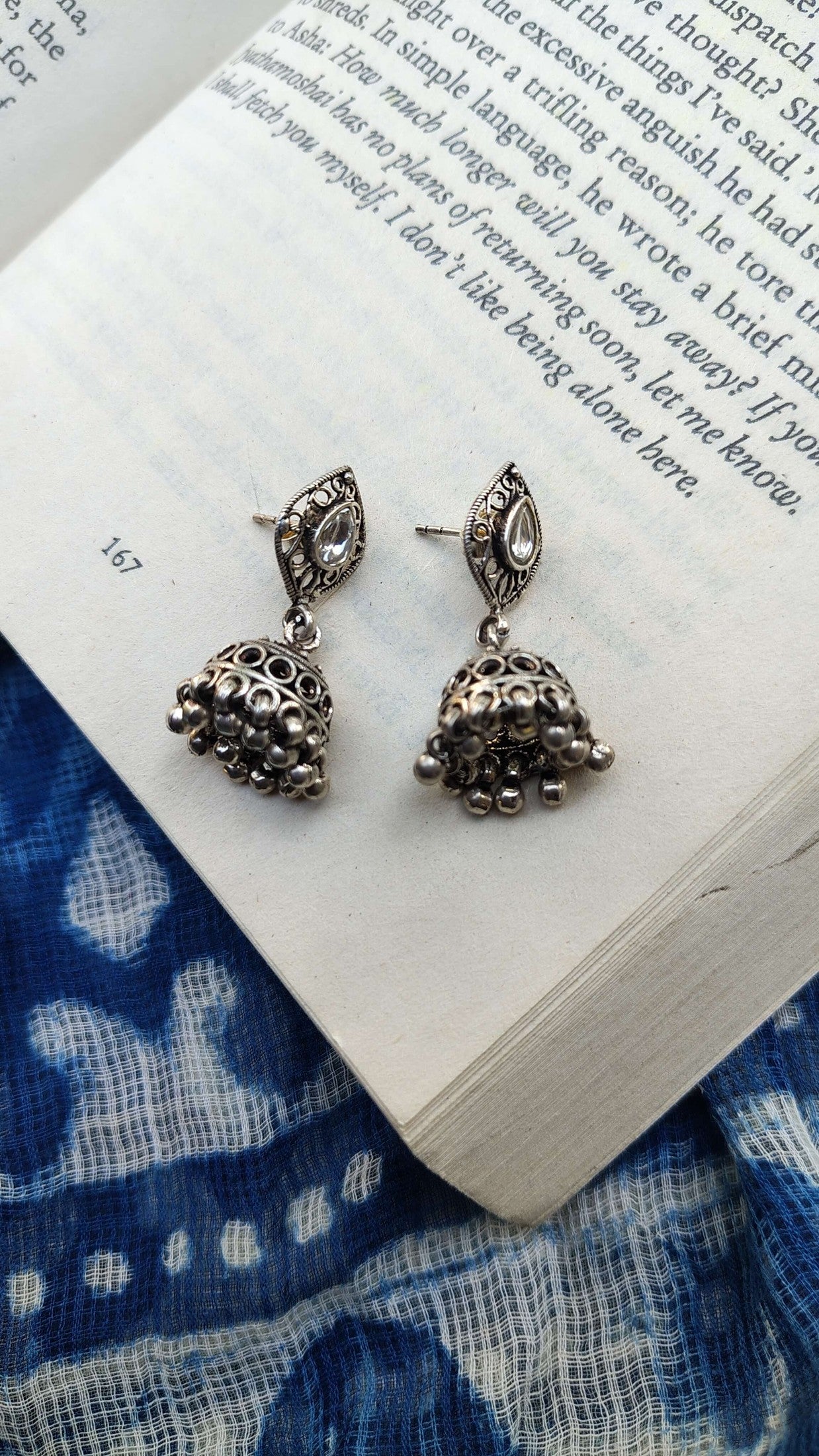 Silver earrings on an open book with a blue fabric background