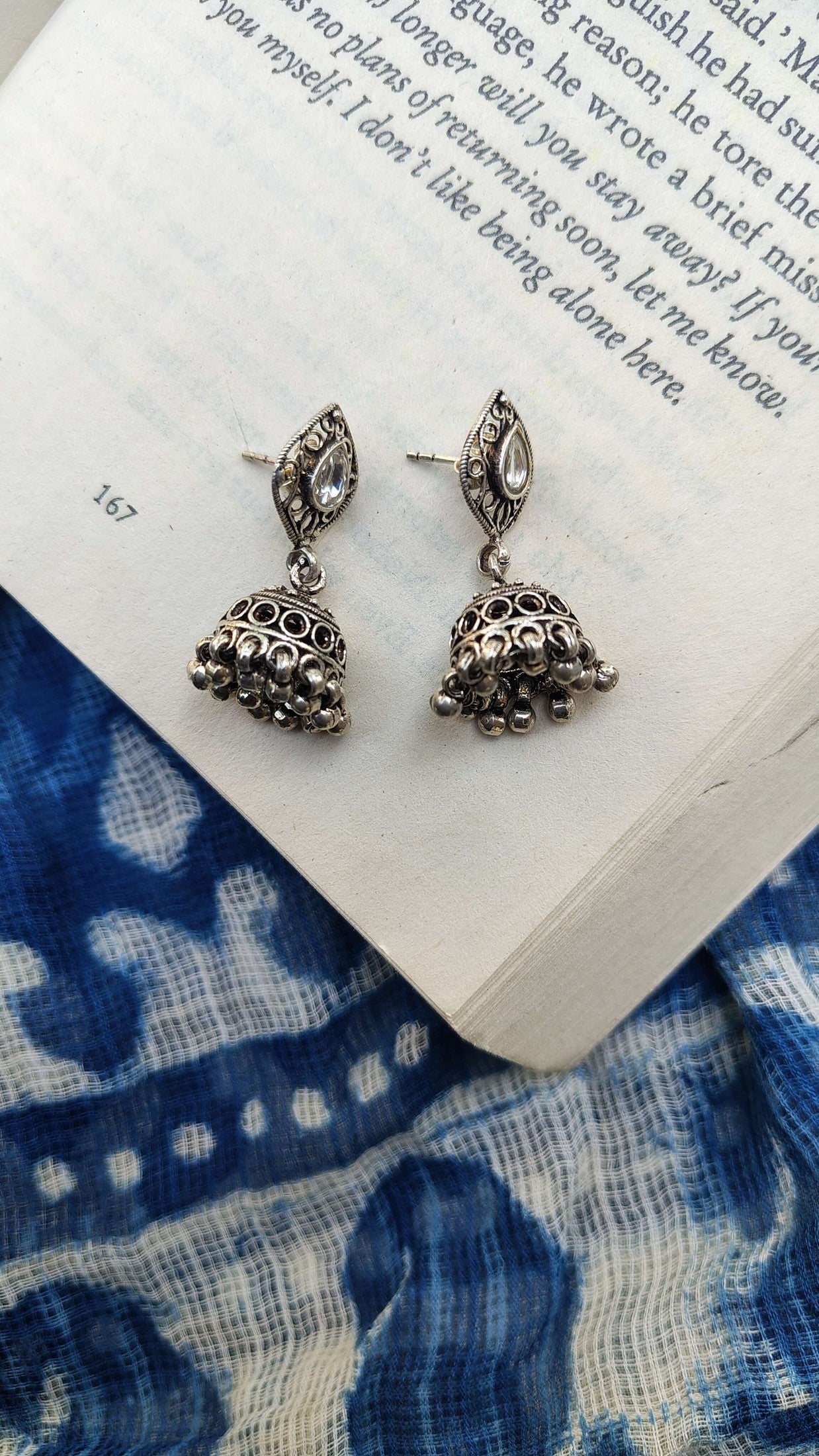 Silver earrings on an open book with a blue patterned fabric background