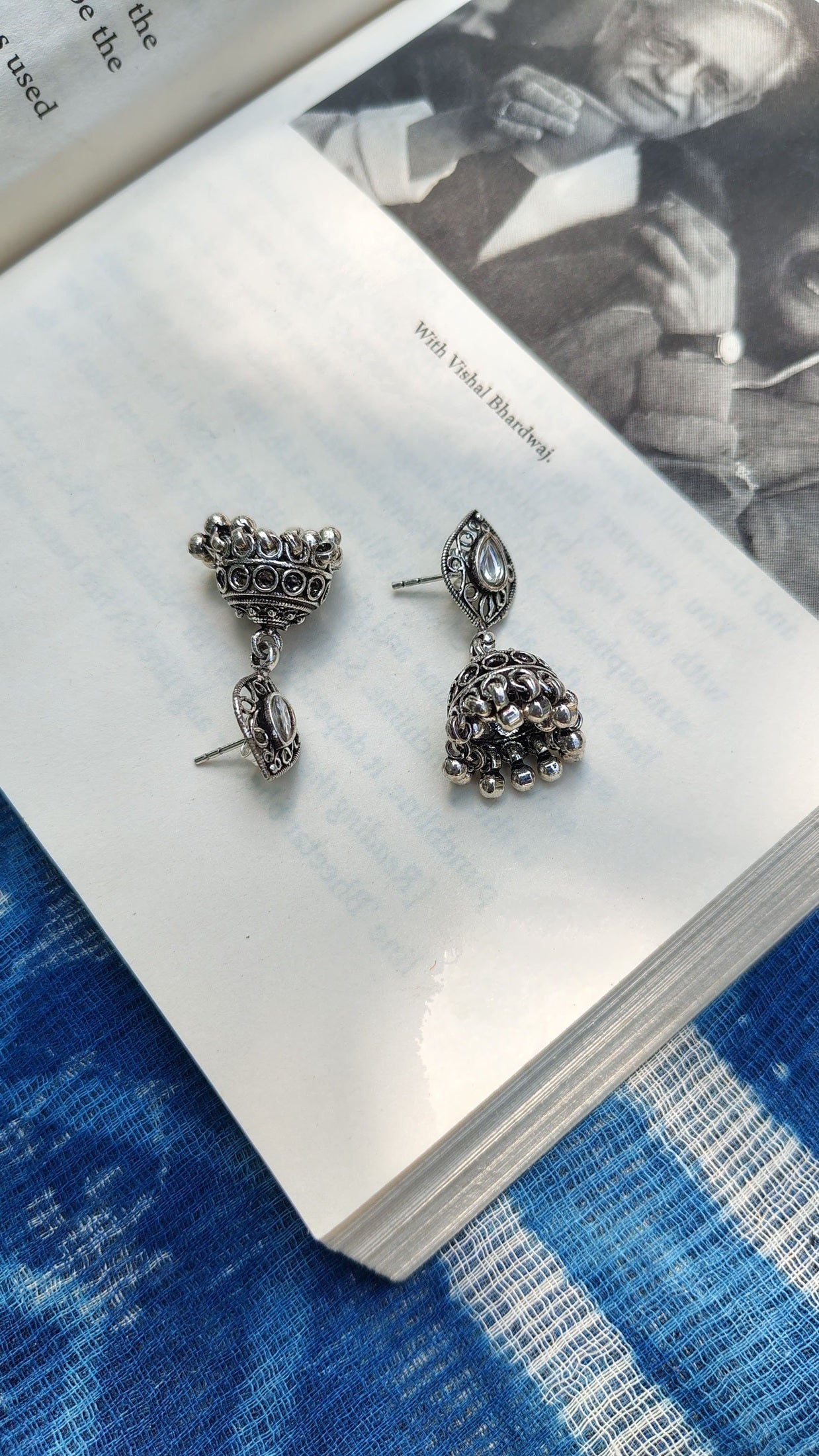 Silver earrings on an open book with a blue fabric background