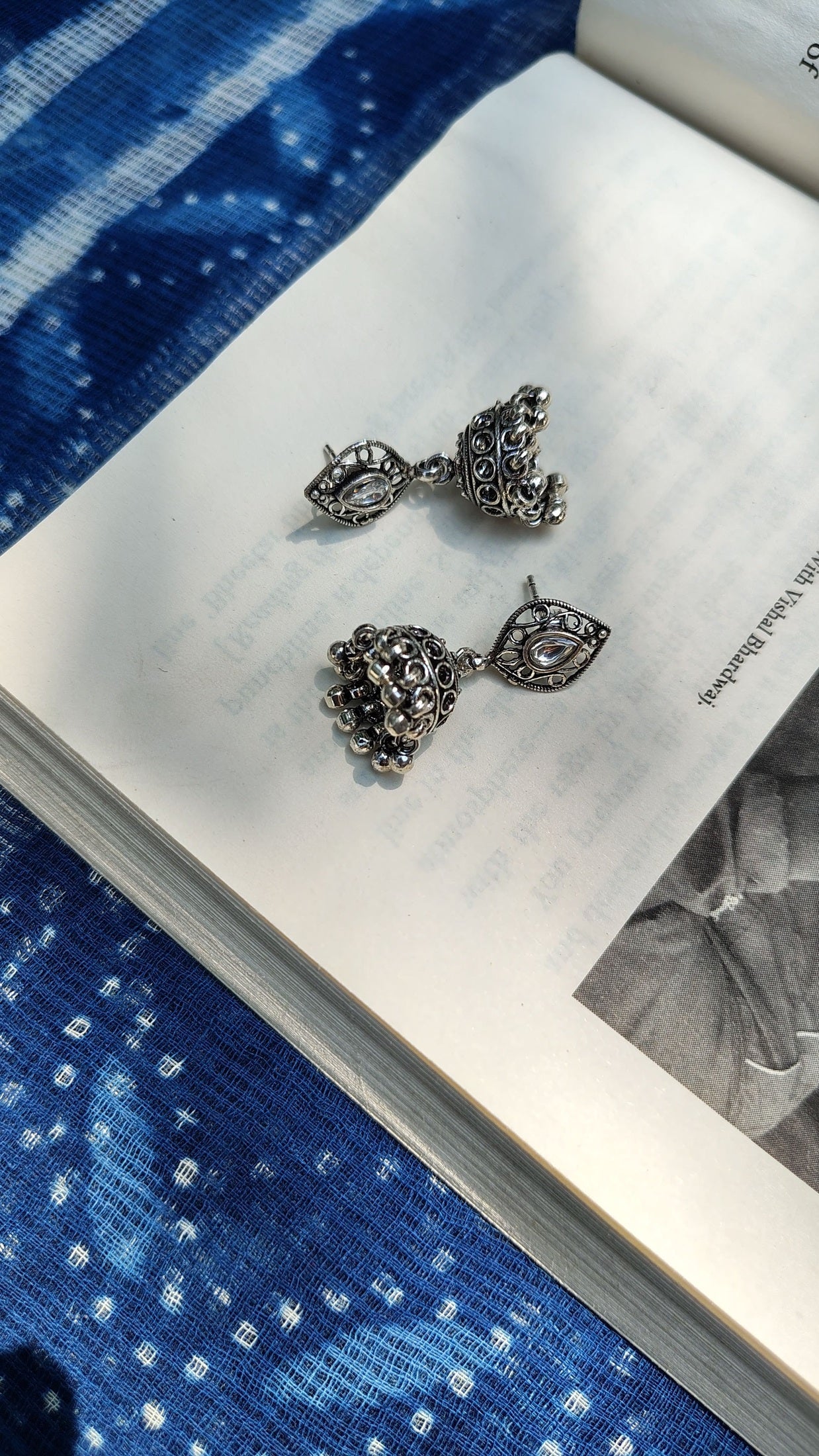 Pair of silver earrings on an open book with a blue fabric background