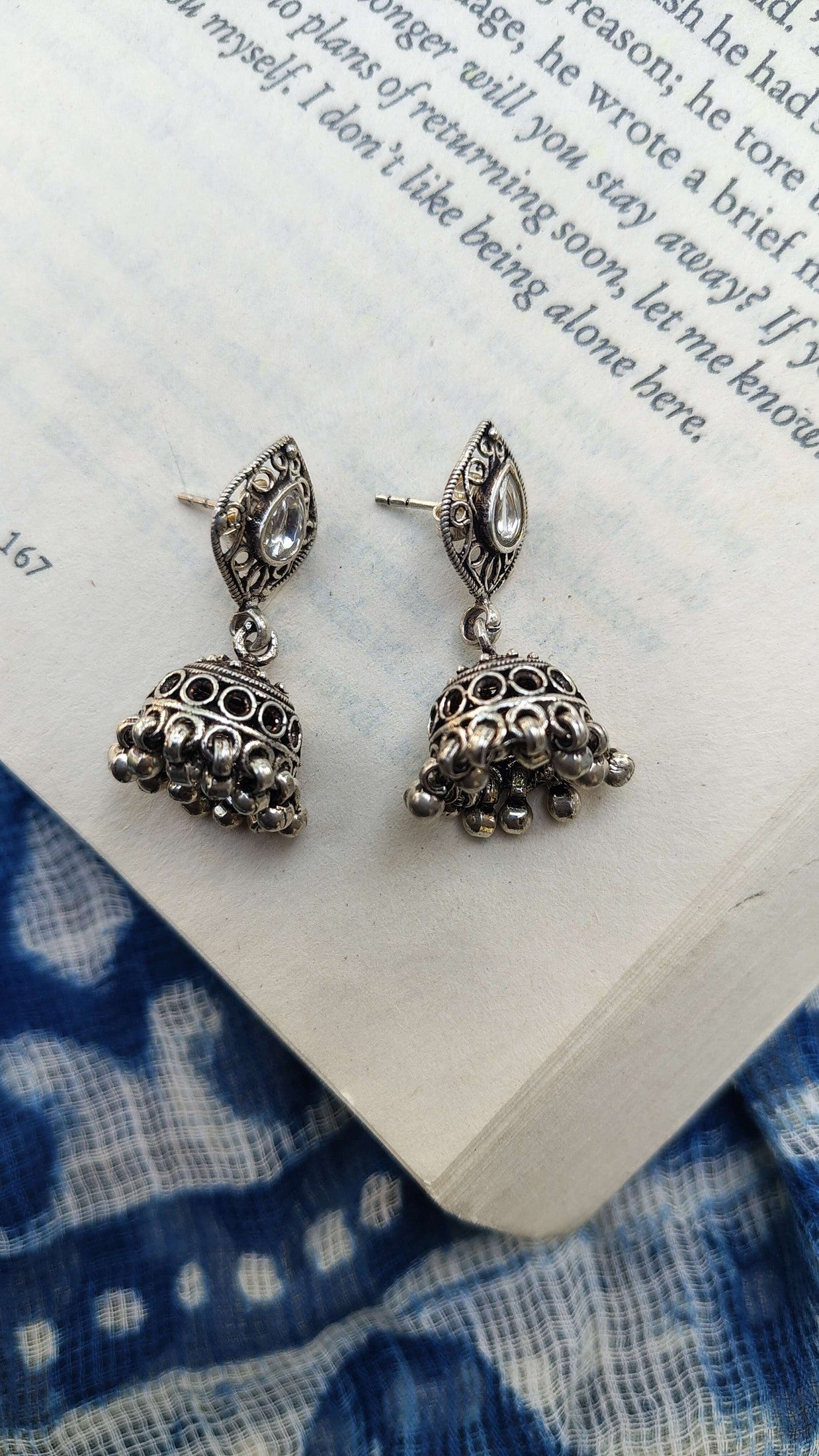 Silver earrings on an open book with blue fabric underneath