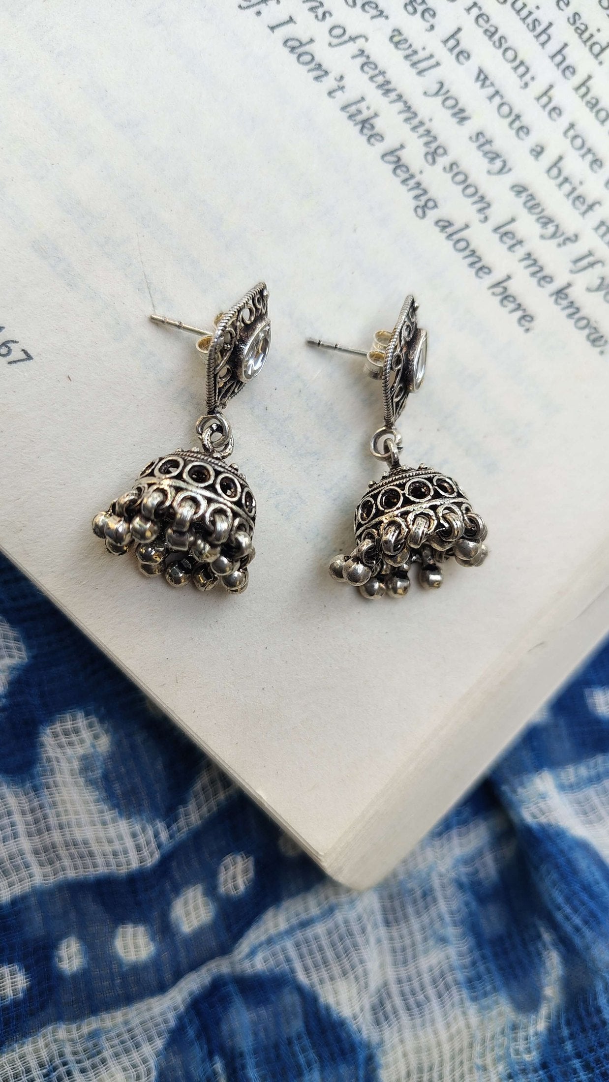 Silver earrings on an open book with blue floral patterns