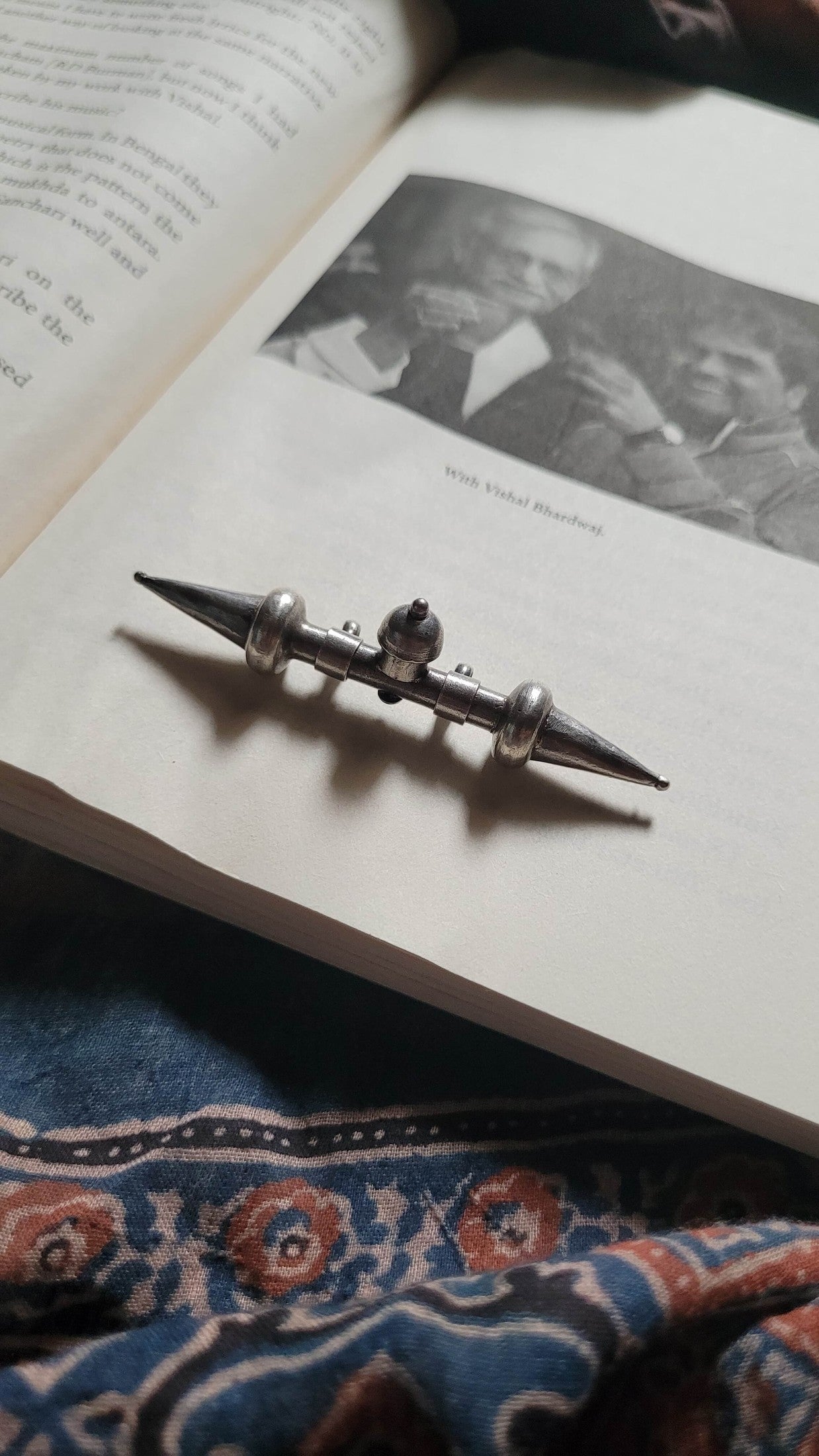 Tavishi Pendant on an open book with a black and white photo of a man.