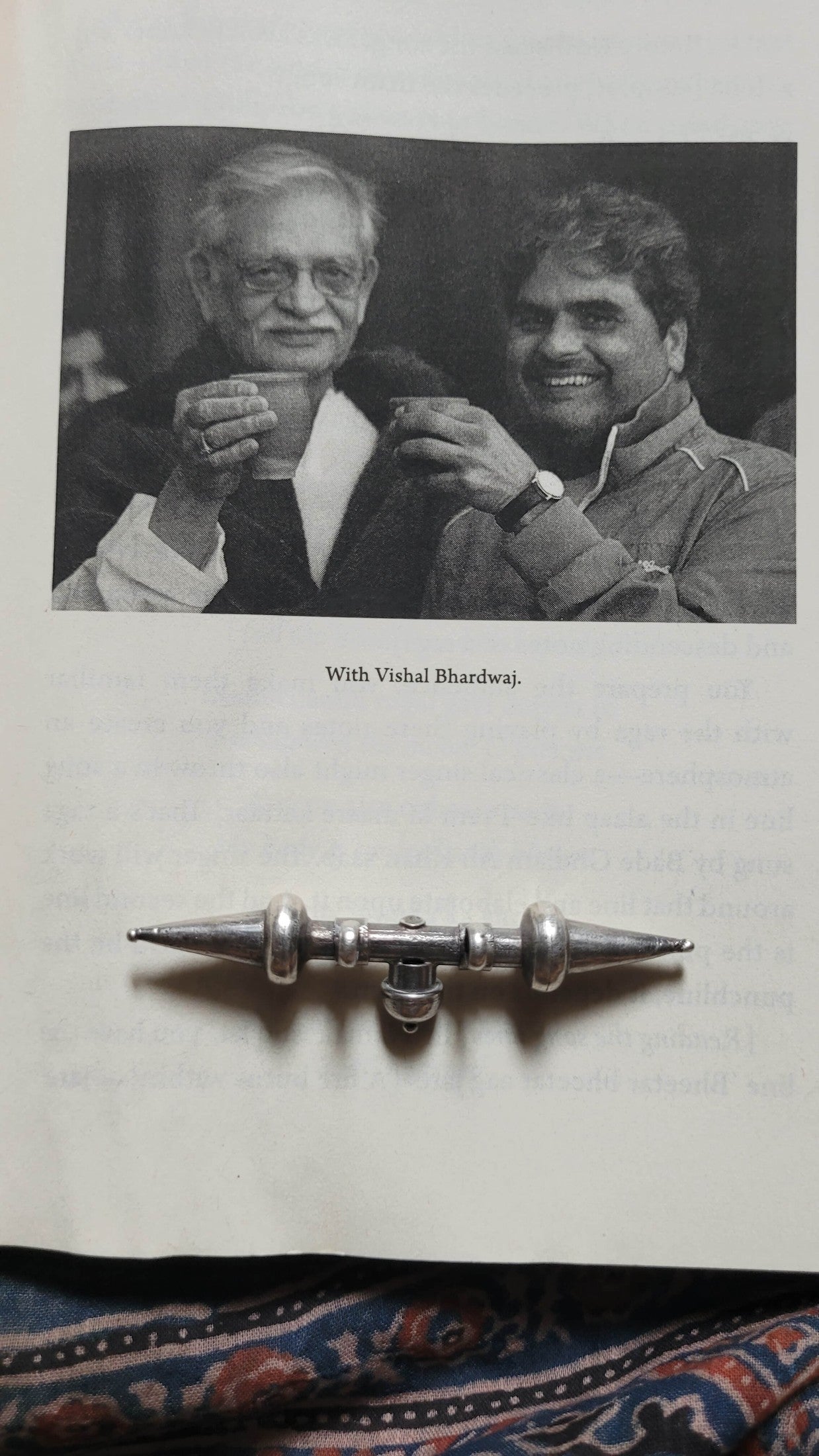 Two men holding cups with the Tavishi Pendant displayed below on a textured surface.