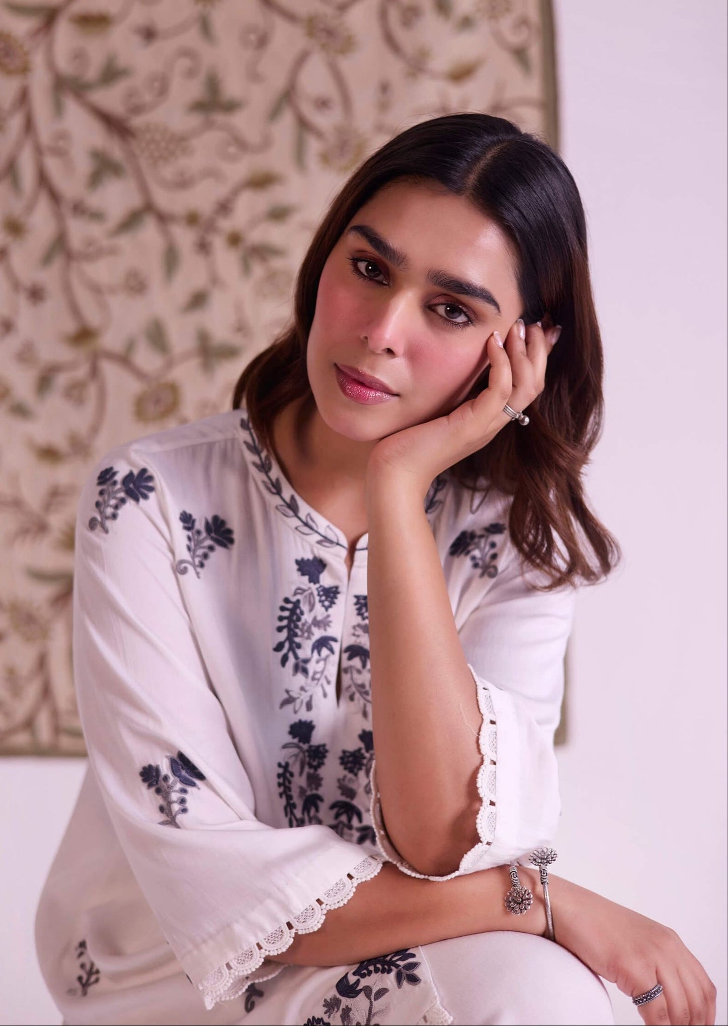 Woman wearing a white embroidered outfit with a decorative wall in the background