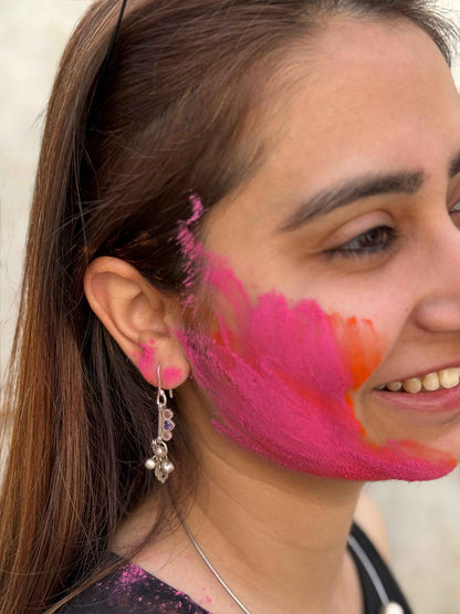 Woman with pink and orange makeup on her face, wearing a silver earring.