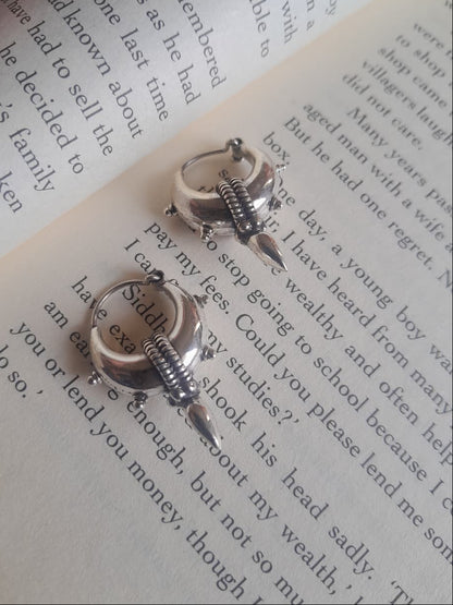 A pair of silver-toned hoop earrings with dangling spring-style charms, photographed resting on printed book pages.