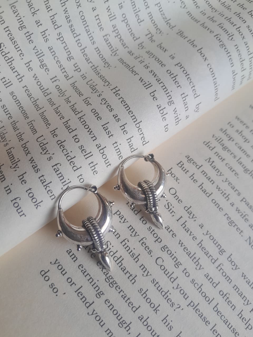 A pair of silver hoop earrings with wing-like dangling charms, displayed on the pages of an open book.