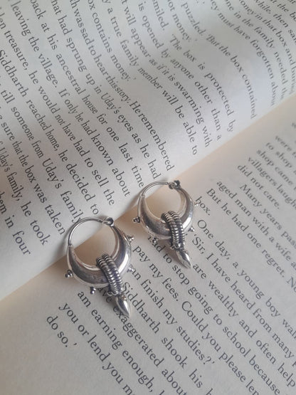A pair of silver hoop earrings with wing-like dangling charms, displayed on the pages of an open book.
