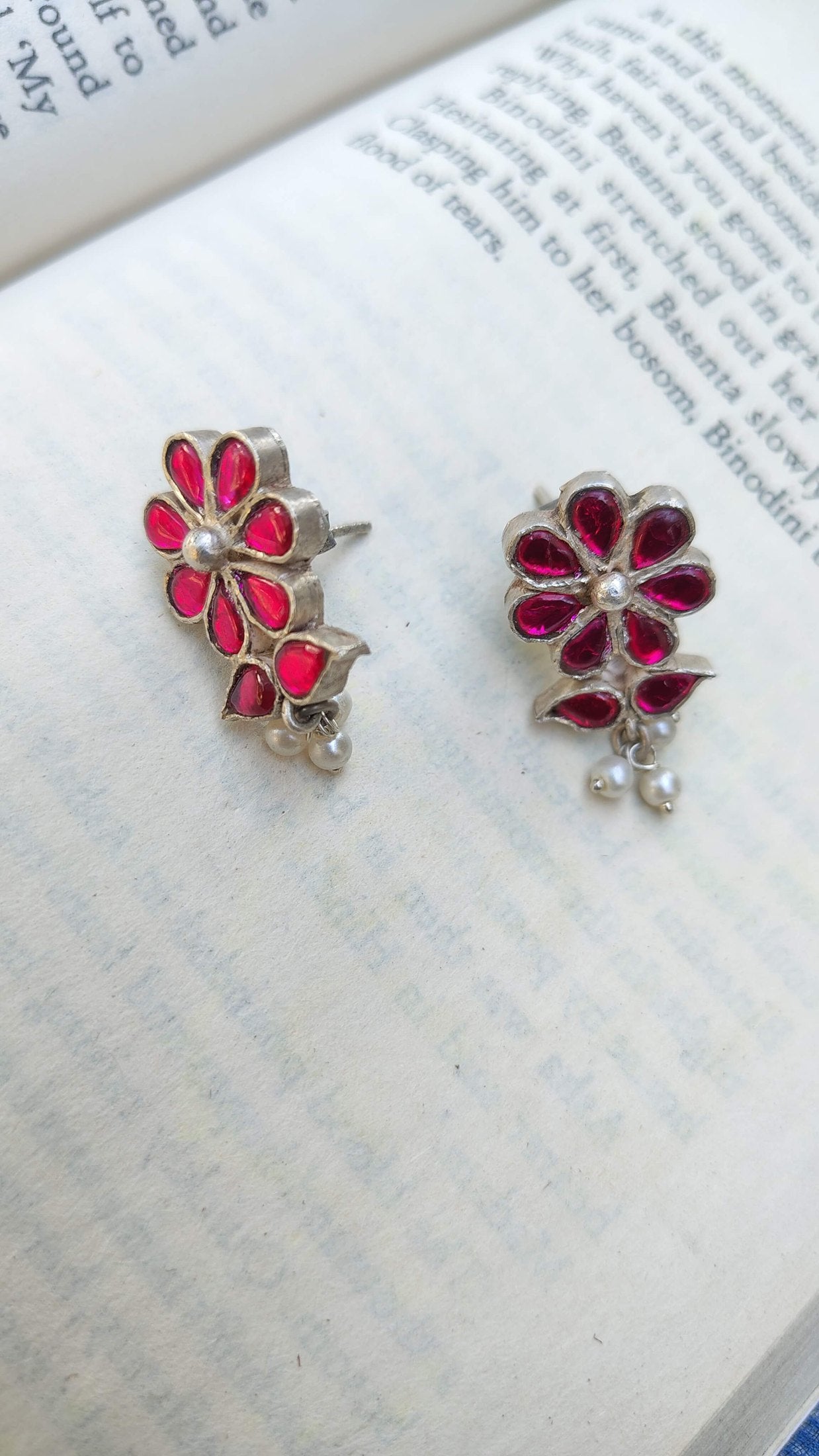 Floral earrings with red centers and silver accents on a book page.