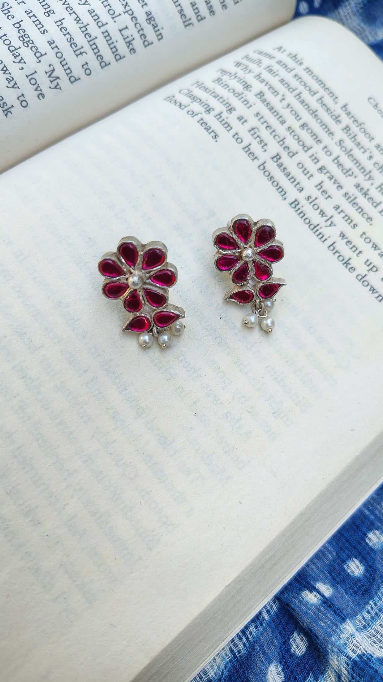Flower-shaped earrings with red stones on an open book