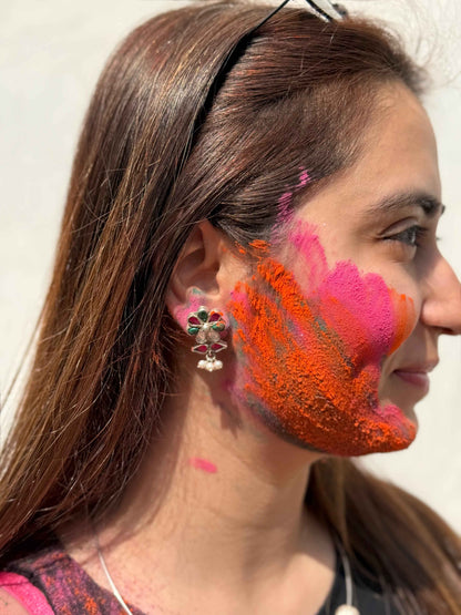 Woman with colorful paint on her face and neck, wearing a headband and silver kundan earrings.