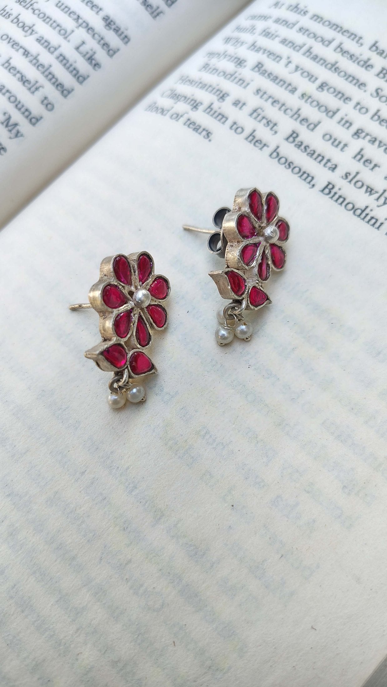 Floral earrings with red and silver design on an open book